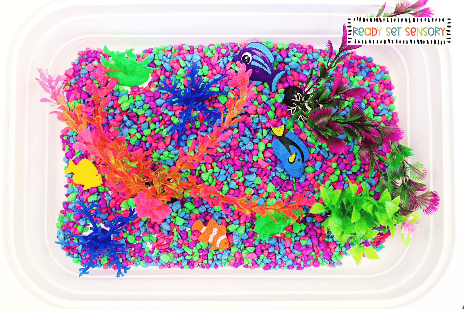 Aquarium sensory bin with colorful rocks, fish, and plants