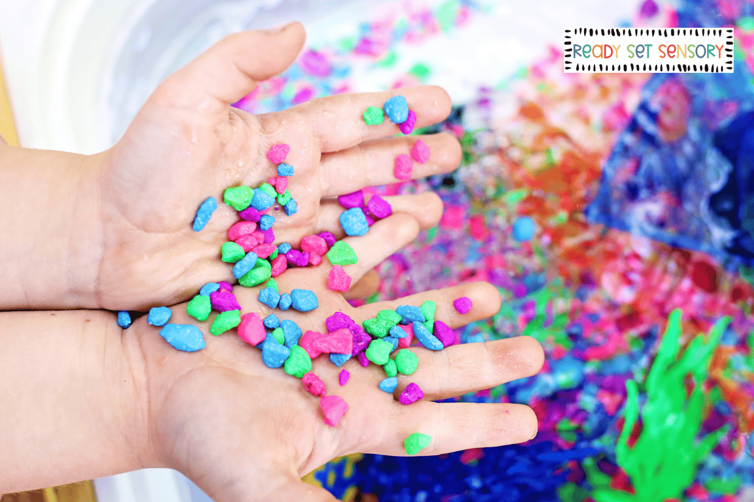 Child holding colorful stones from aquarium sensory bin