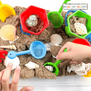 Beach sensory bin activity with sand, shells, and fine motor tools