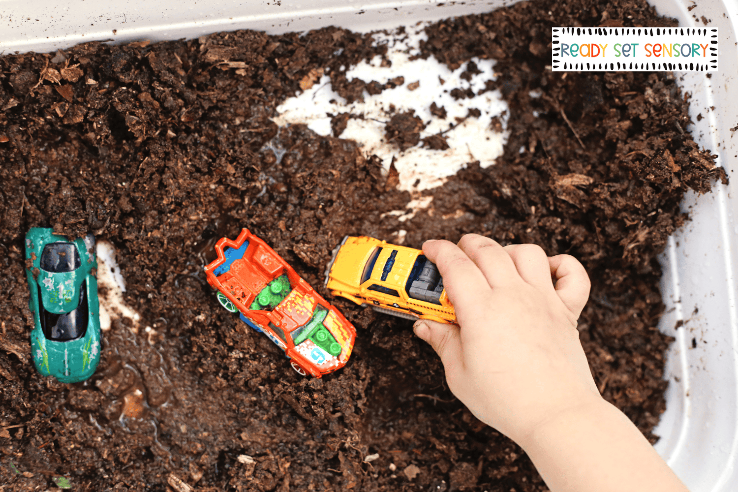 Child washing toy cars in muddy car wash sensory bin