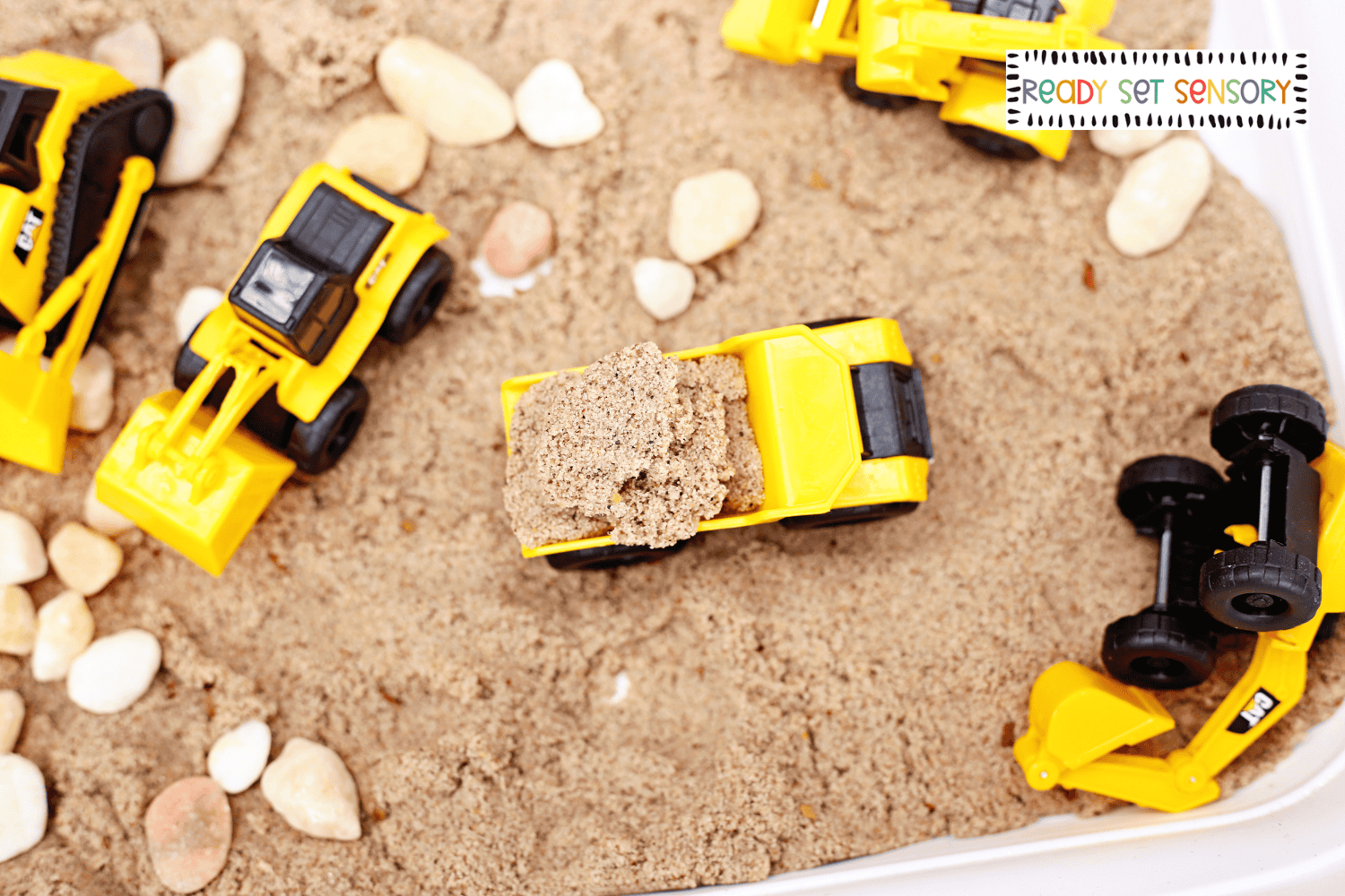 Toy dump truck carrying sand in construction site sensory bin