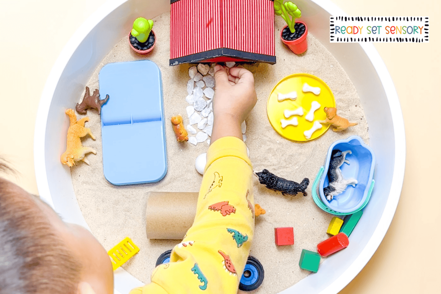 toddler playing with dog park sensory bin using toy dogs and sand