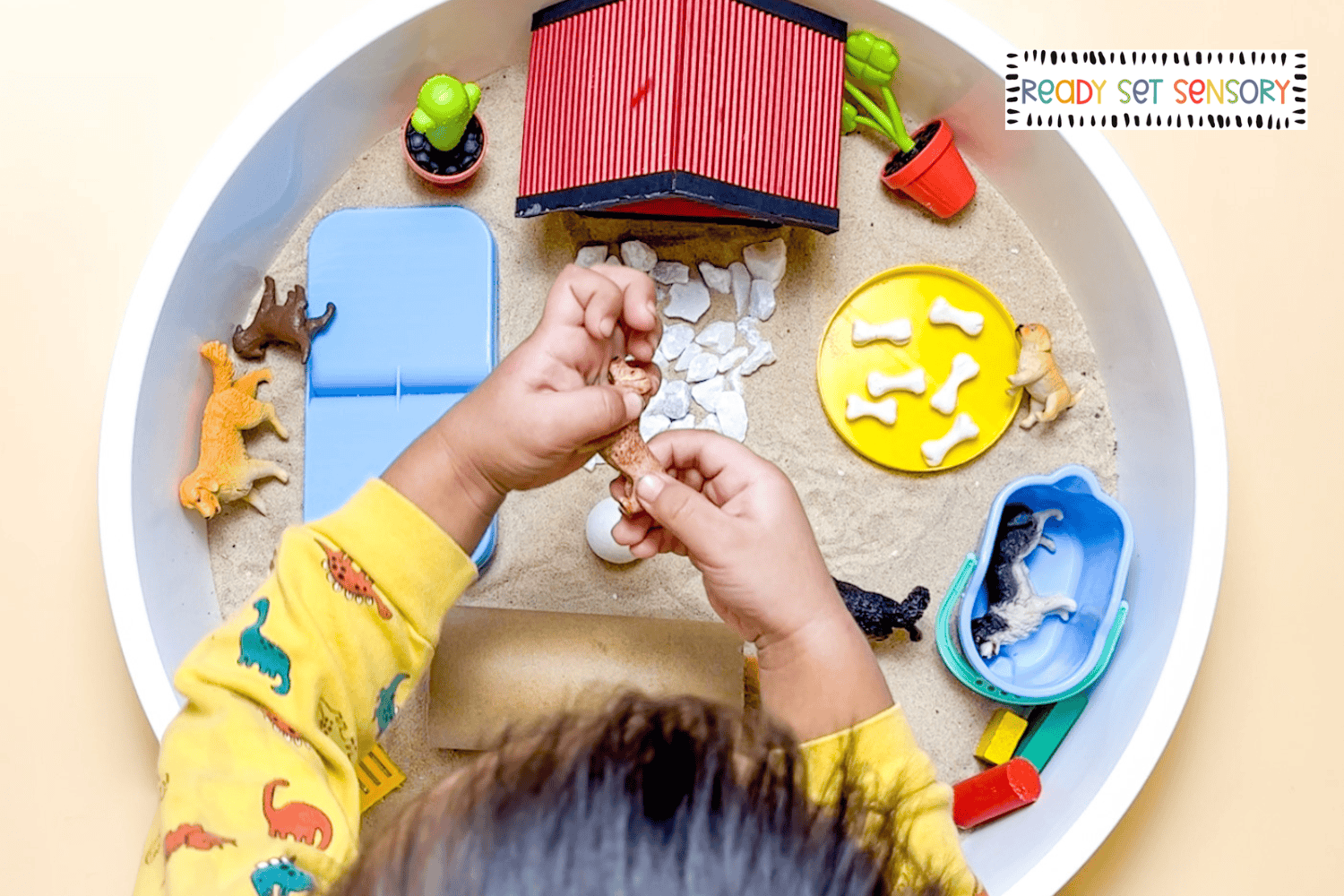 child exploring dog park sensory bin with toy dogs and pretend kennel