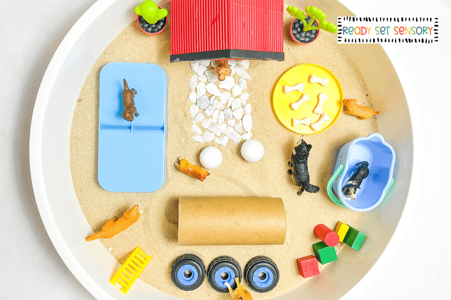 dog park sensory bin supplies including toy dogs, sand, bowls, and blocks