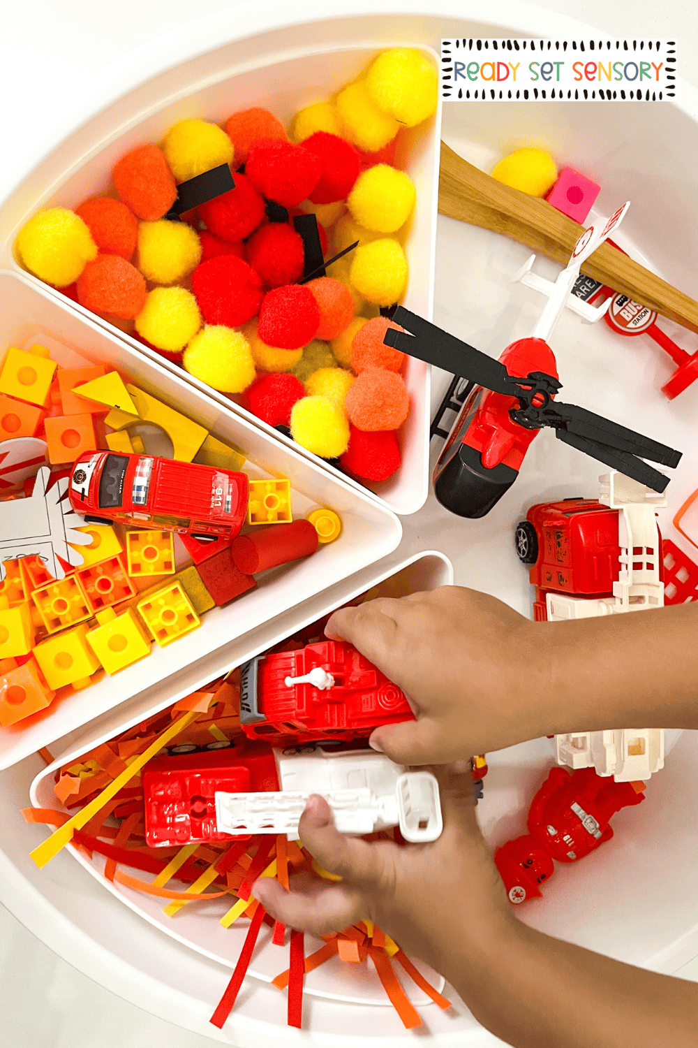 Hands playing with fire rescue sensory bin using toy fire engines and tools