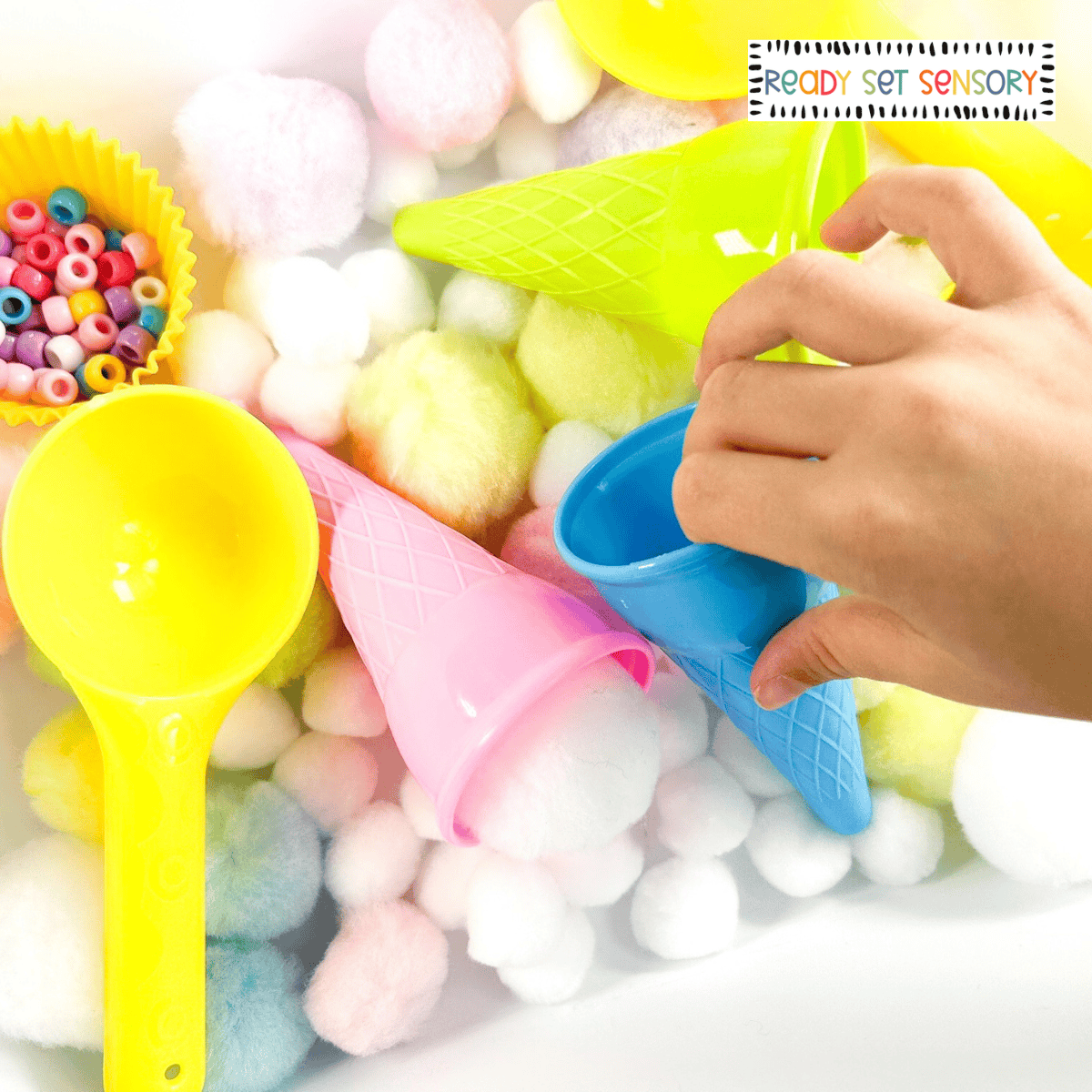 Ice cream sensory bin with colorful pom poms, cones, and fine motor tools