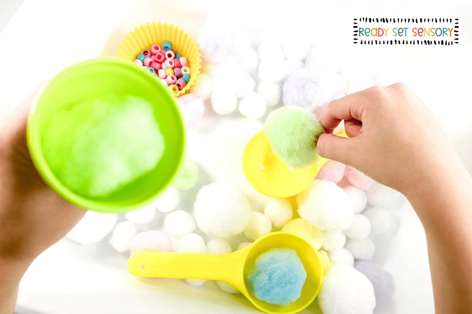 Toddler transferring pom poms using scoops in an ice cream sensory bin