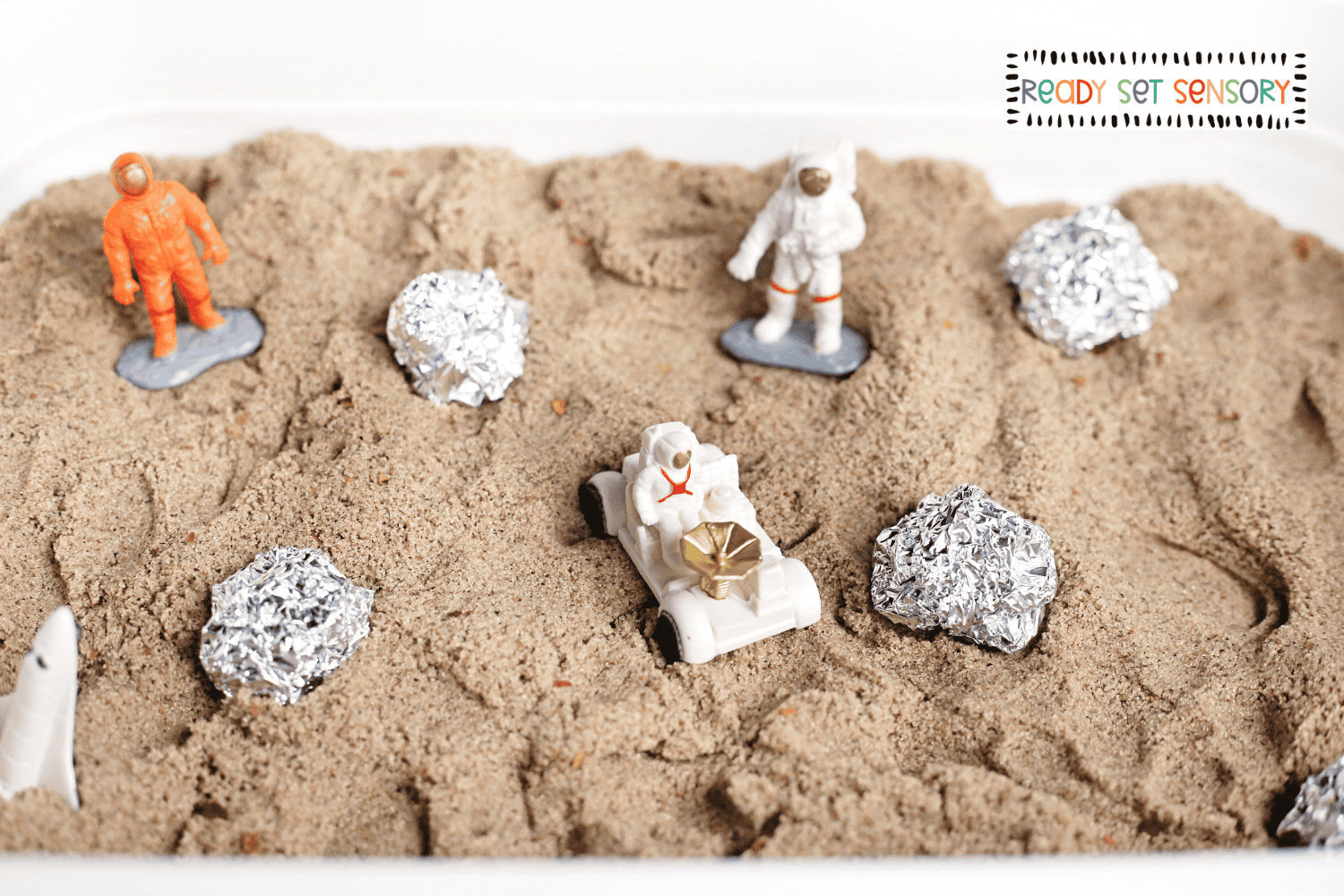 Moon landing sensory bin with toy astronauts exploring a sandy moon surface