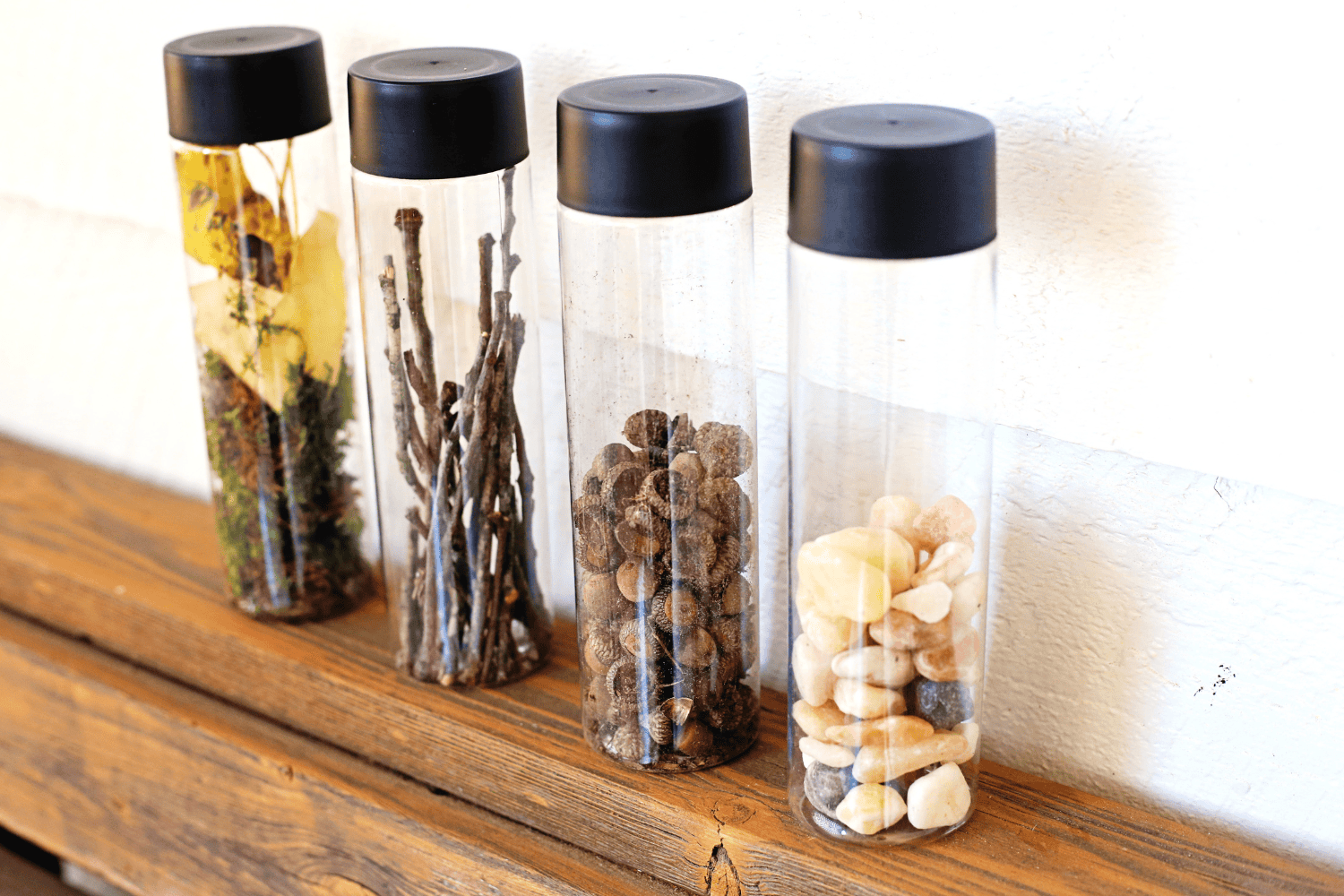 Nature sensory bottles lined up with pebbles, sticks, and acorns
