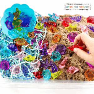 Seashell sensory bin with colorful shells, sand, and fine motor play materials