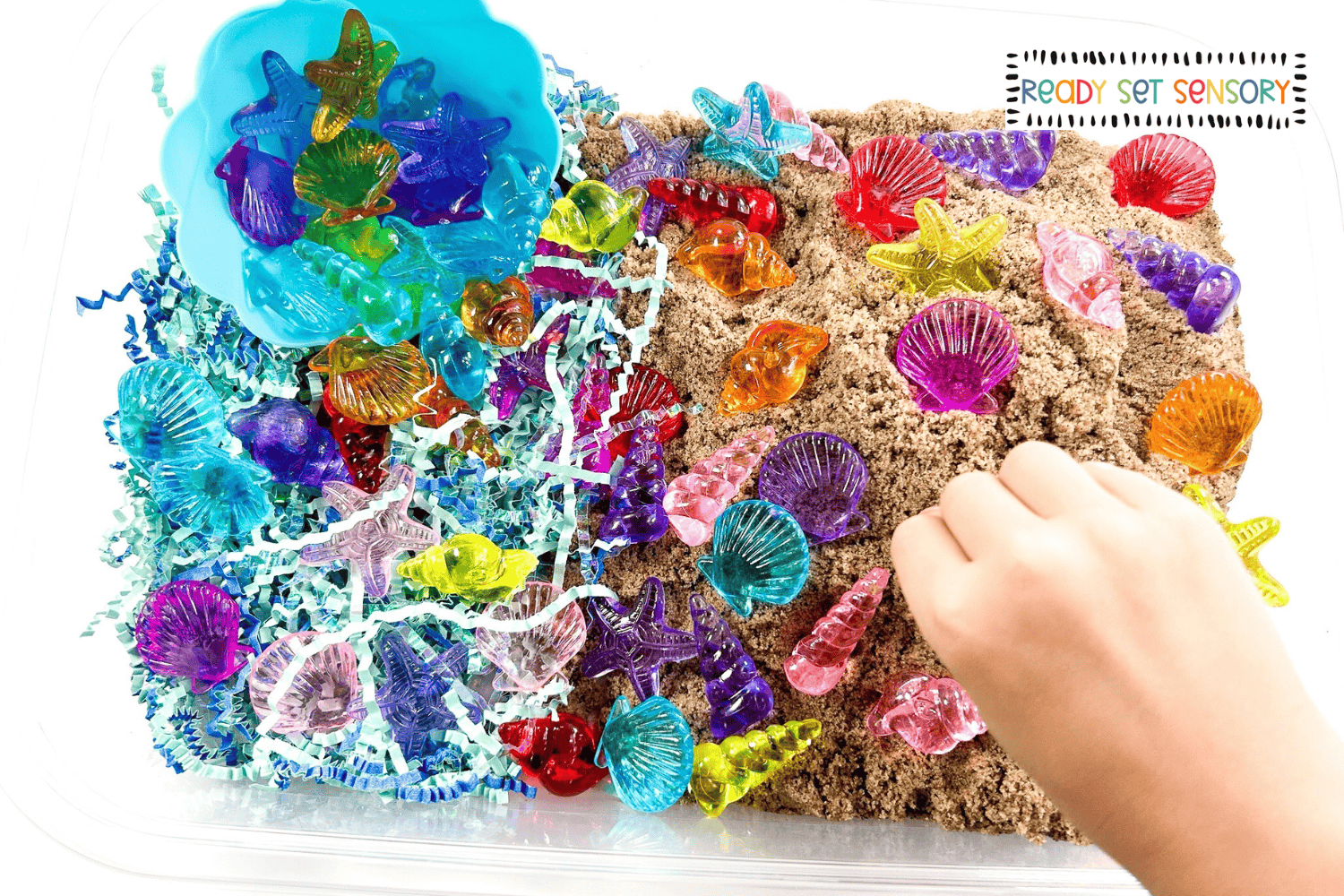 Toddler playing with a seashell sensory bin using sand and bright shell shapes
