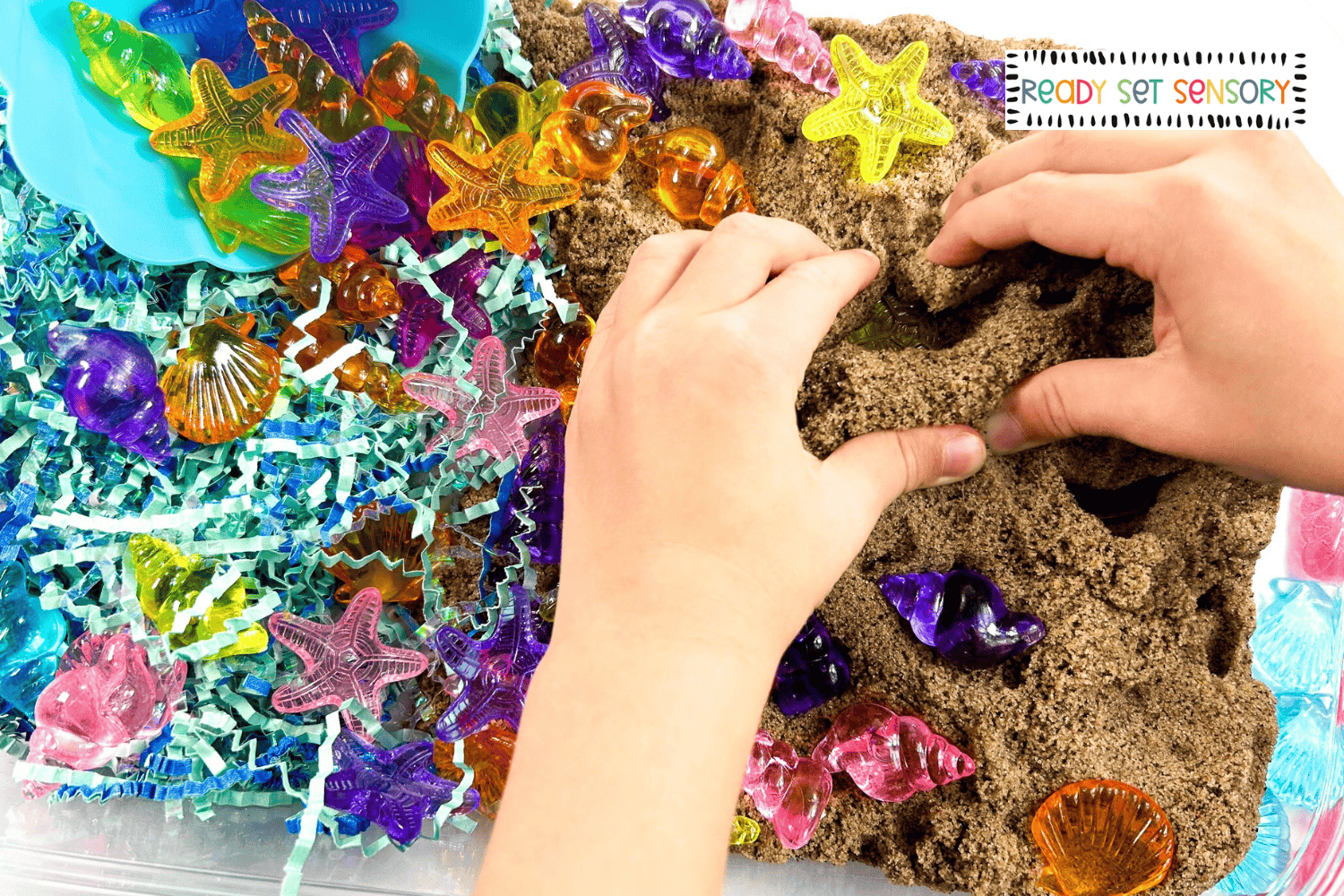 Child exploring a seashell sensory bin with kinetic sand and colorful plastic shells