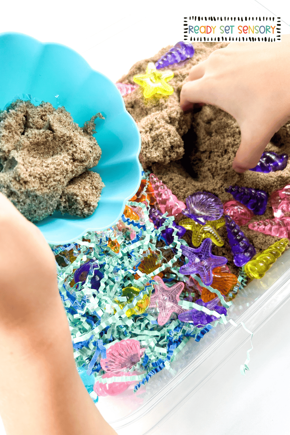 Hands scooping kinetic sand in a seashell sensory bin activity for kids