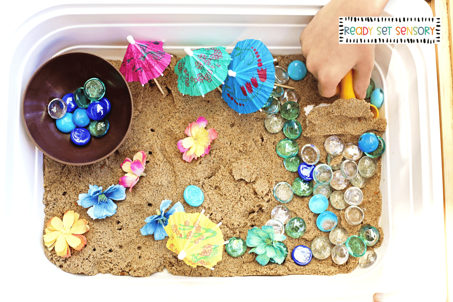 Child scooping sand and gems in tropical sensory bin