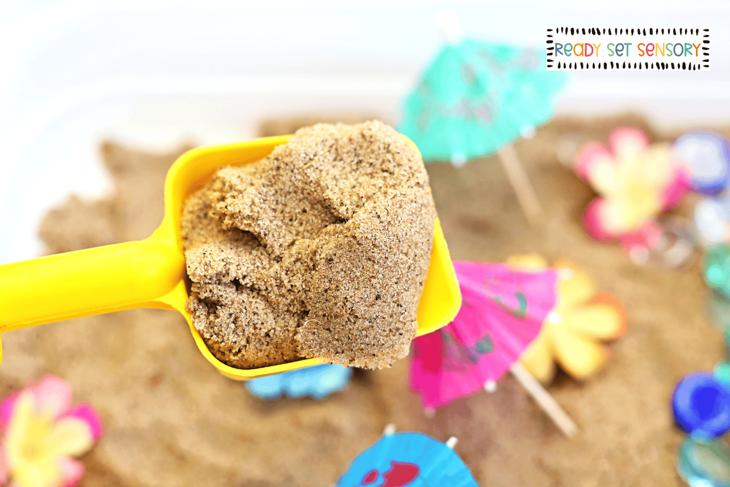 Yellow scoop filled with sand in tropical sensory bin