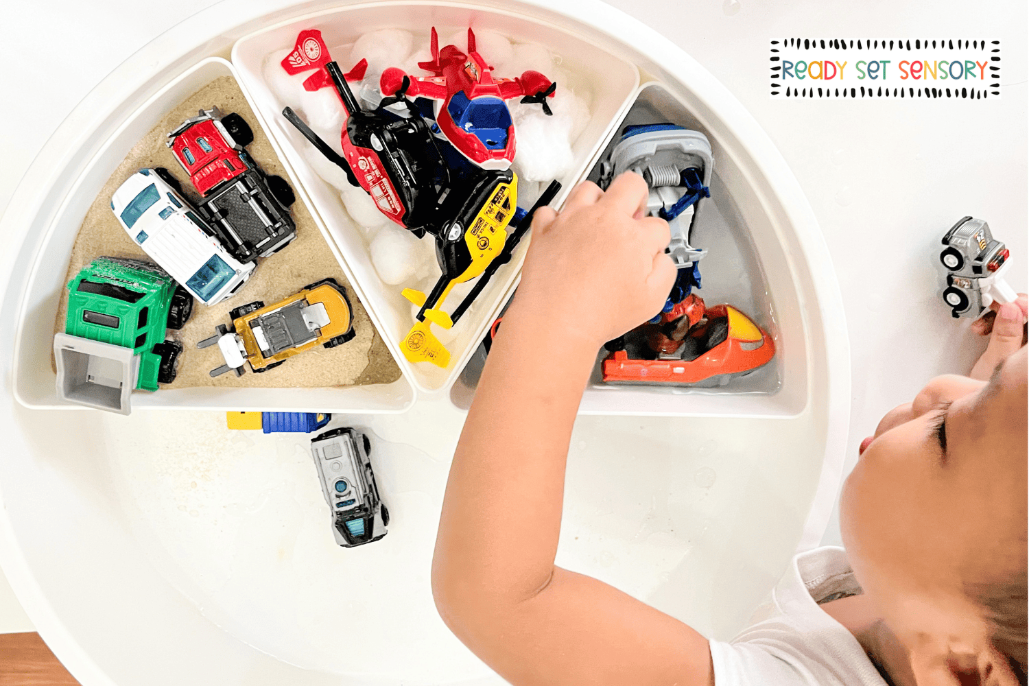 Toddler sorting toy cars, trucks, and helicopters in sensory bins