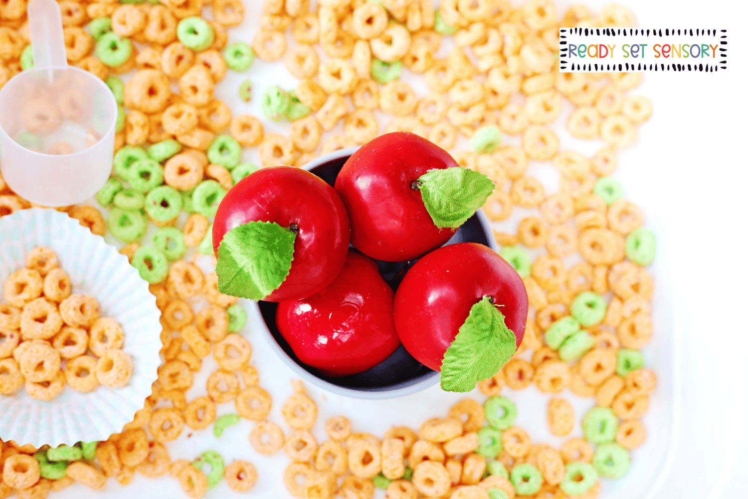 Apple Jacks sensory bin activity with red apples and cereal in bowl for fine motor play