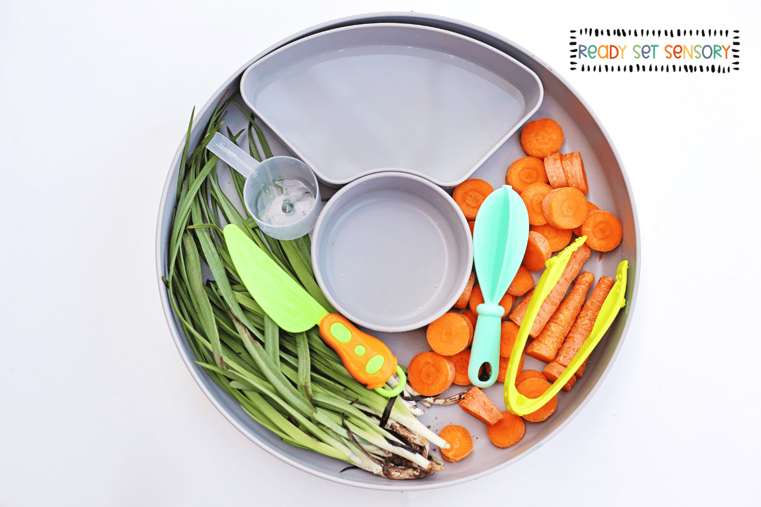Bunny Bait sensory bin setup with carrots, green grass, and toddler tools