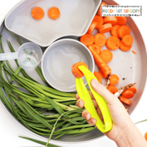 Child using tongs to pick up carrots in Bunny Bait sensory bin