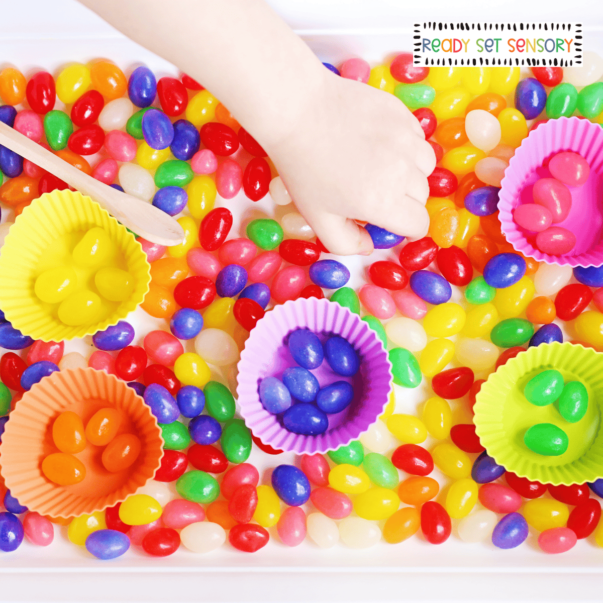 Child sorting colorful jelly beans into cups in jelly bean color sorting sensory bin